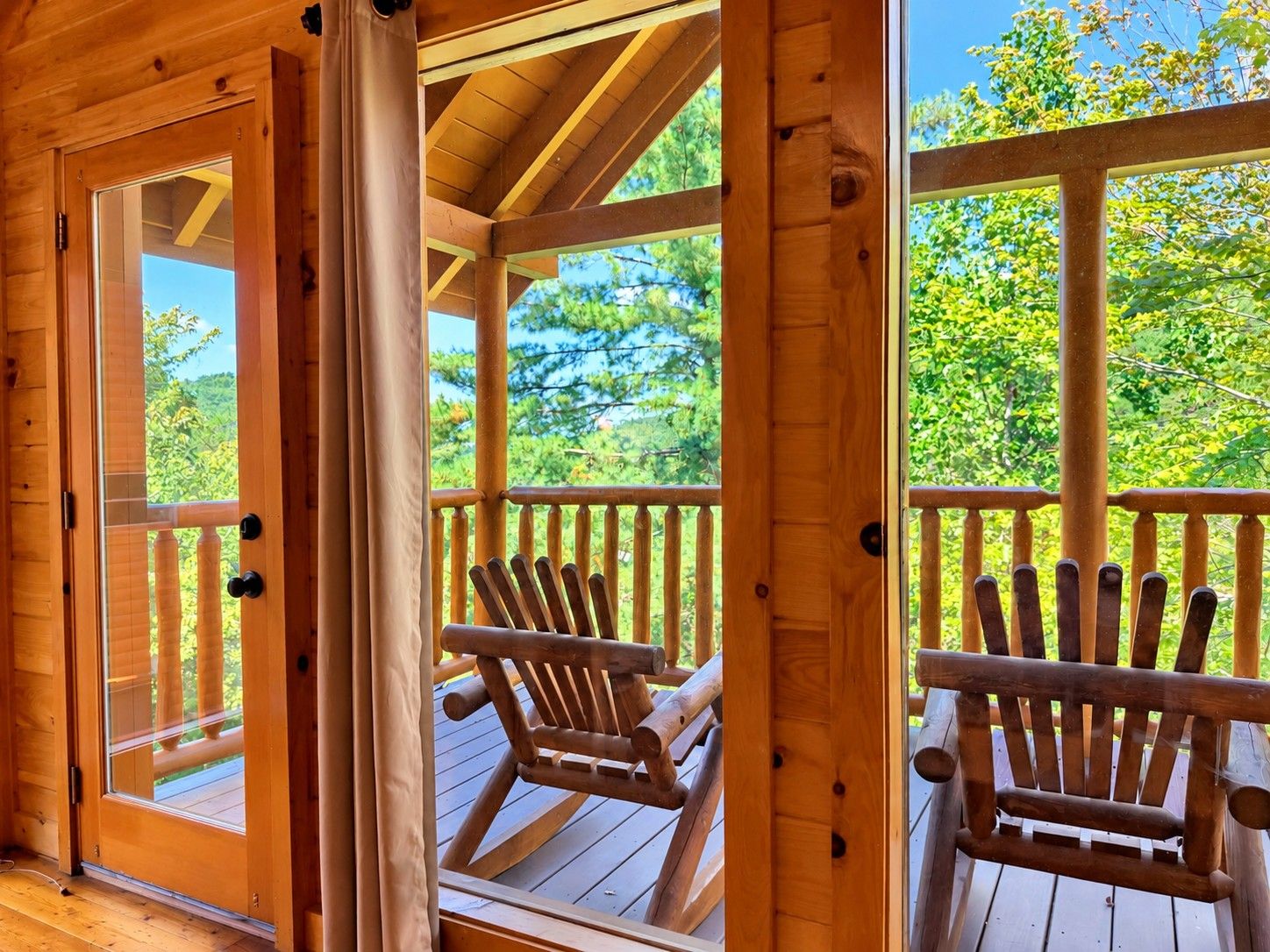A wooden deck with two Adirondack chairs, a wooden railing, and a view of trees and sky.