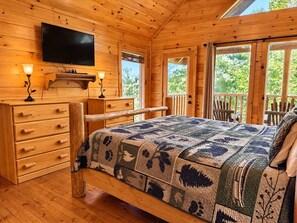 A wooden cabin bedroom with a bed, dresser, and TV.