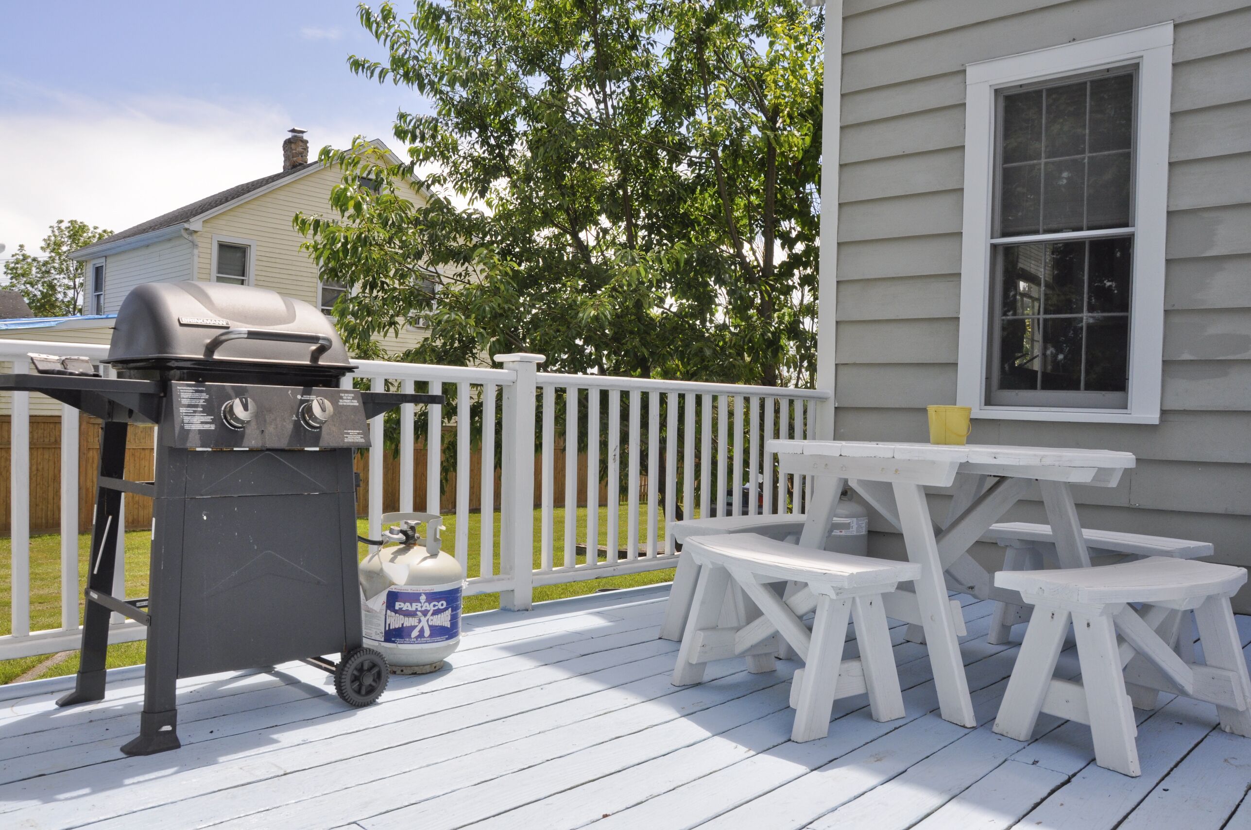 A deck with a barbecue grill, a propane tank, and picnic tables.