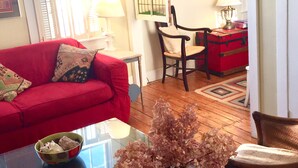 Ein Wohnzimmer mit einem roten Sofa, einem Glastisch mit einer Vase, Holzboden und einer Tür zu einem anderen Raum.