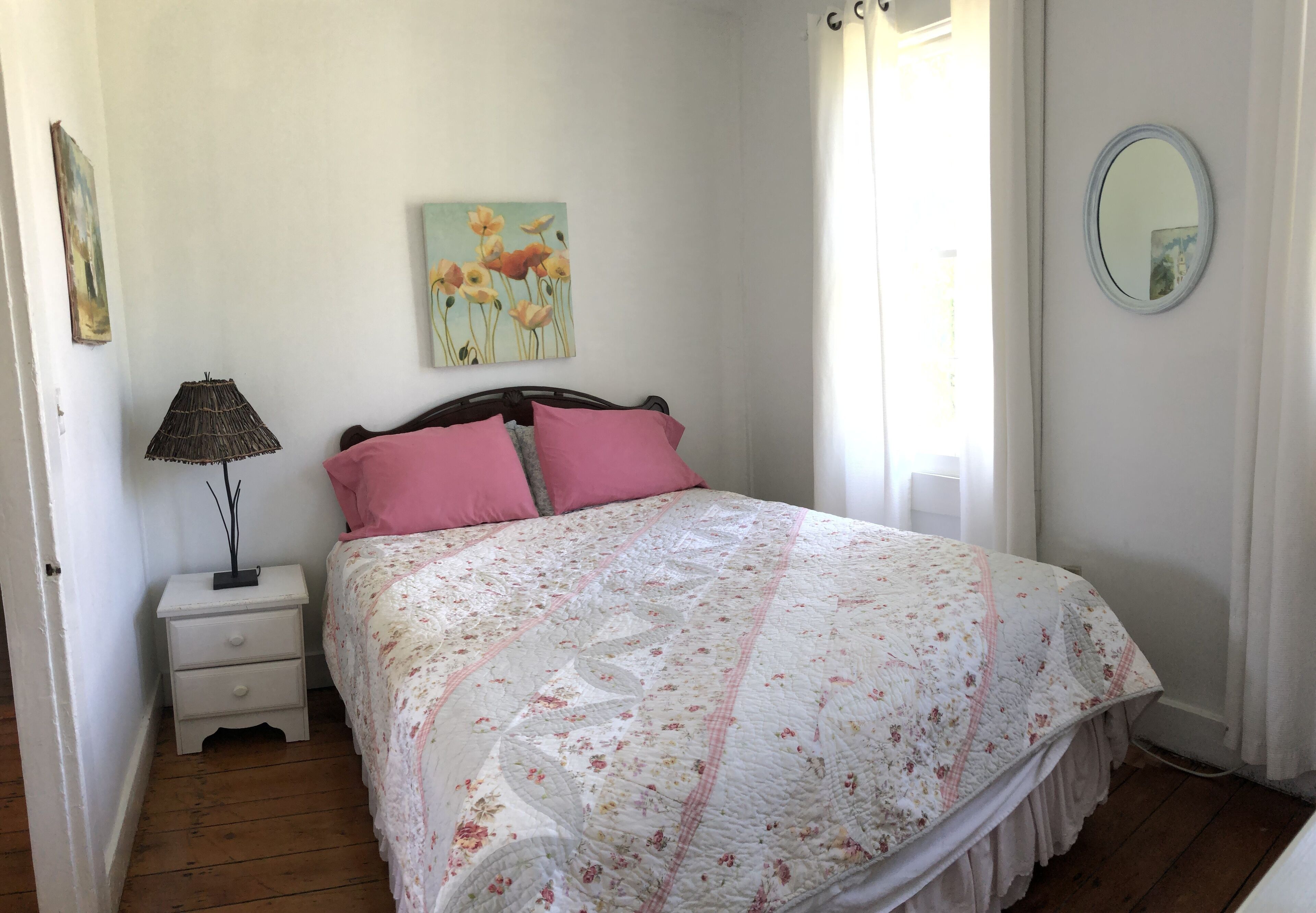 Un dormitorio con cama, mesita de noche, lámpara, cuadro y espejo.