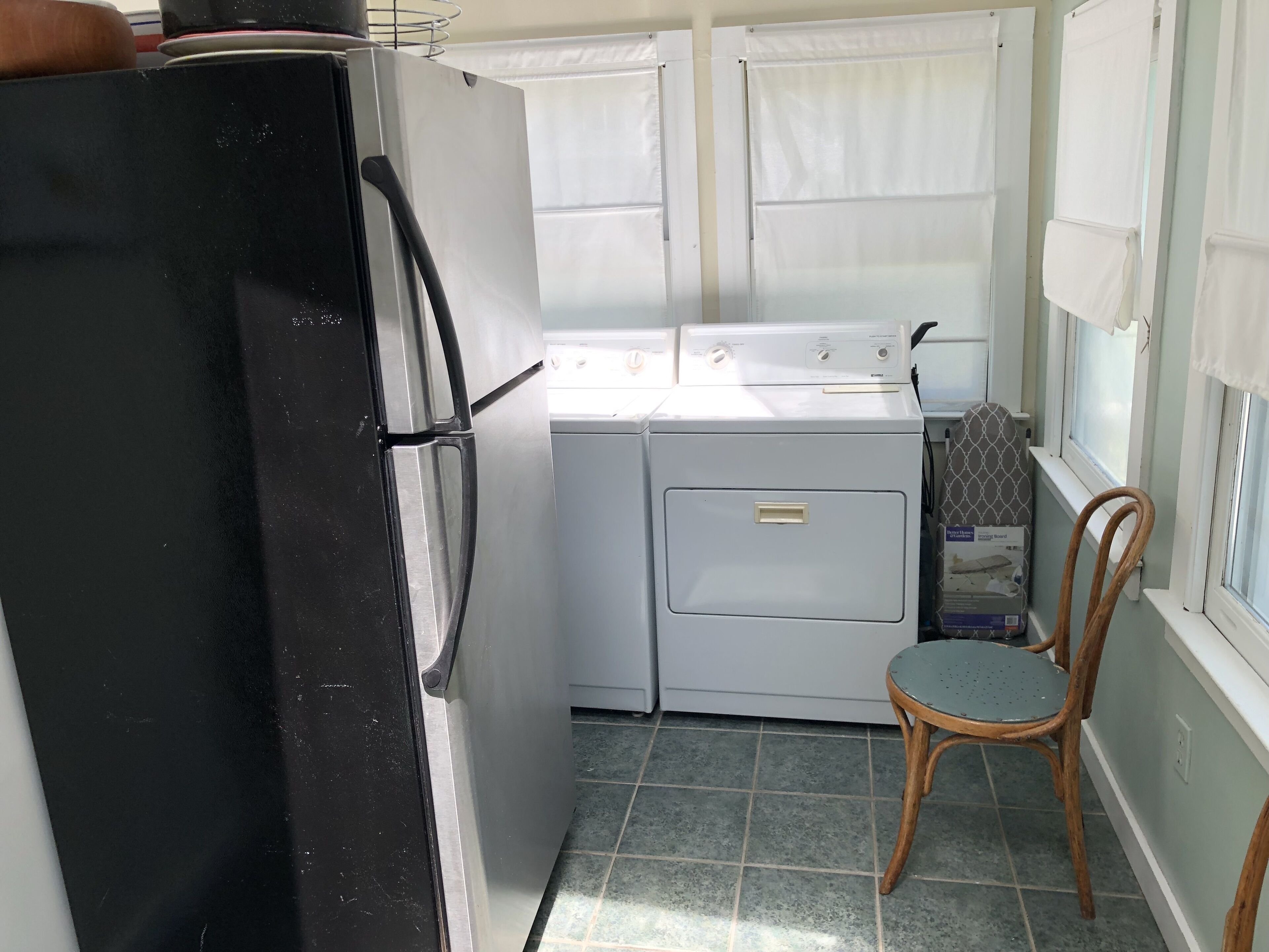A compact kitchen with a black refrigerator, a washing machine, and a wooden chair.