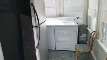 A compact kitchen with a black refrigerator, a washing machine, and a wooden chair.