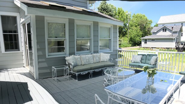 Eine überdachte Terrasse mit einem Glastisch, weißen Metallstühlen, einem grünen Sofa und einer weißen Metallbank.