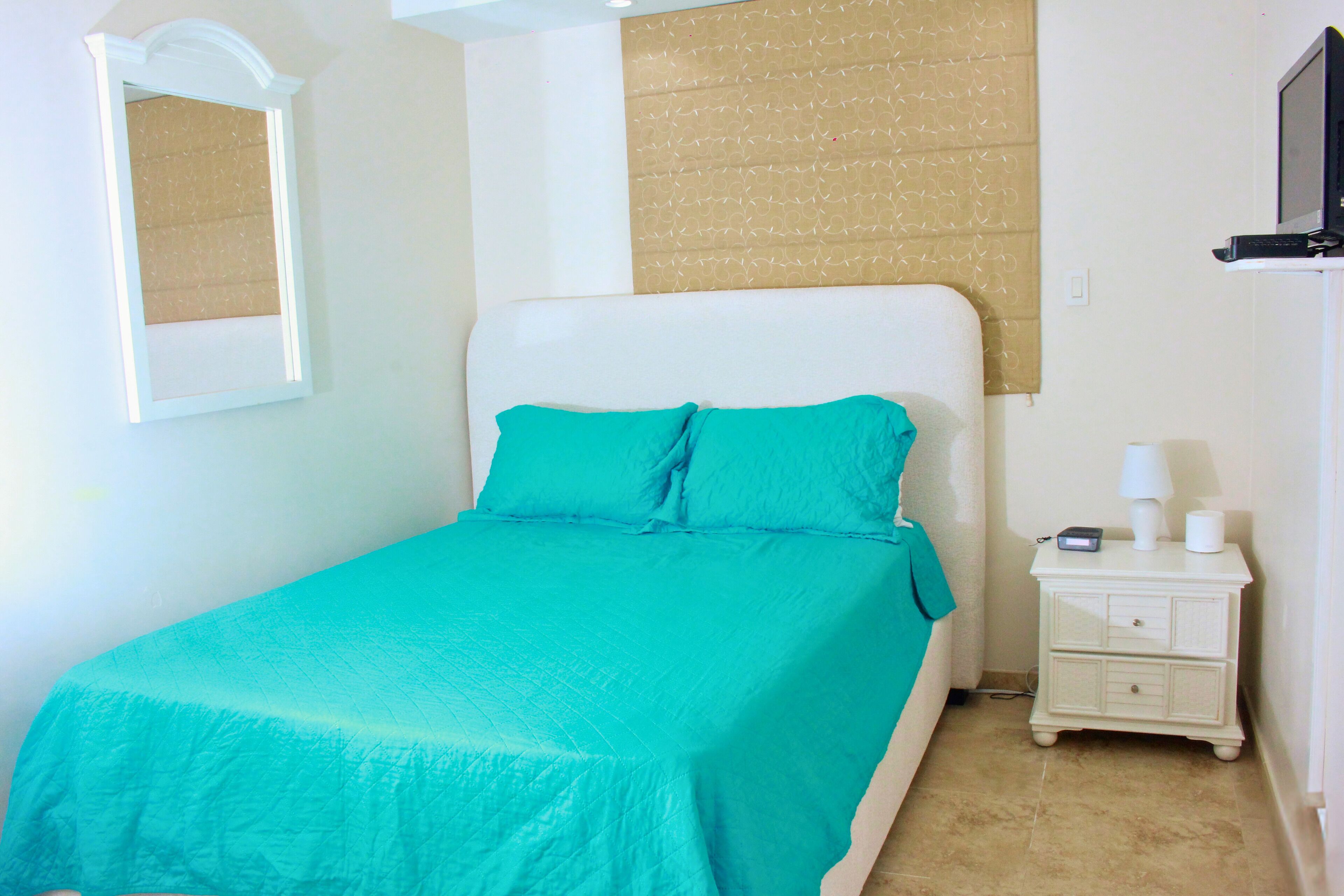 A bedroom with a bed, a nightstand, a television, and a window with blinds.
