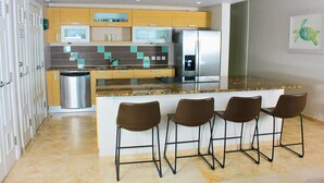 A modern kitchen with a central island, bar stools, stainless steel appliances, and a tiled backsplash. - White Sand Beach Front, Turquois Blue Ocean View, Pools, Hot tub, Guarded,5 star (Christ Church)