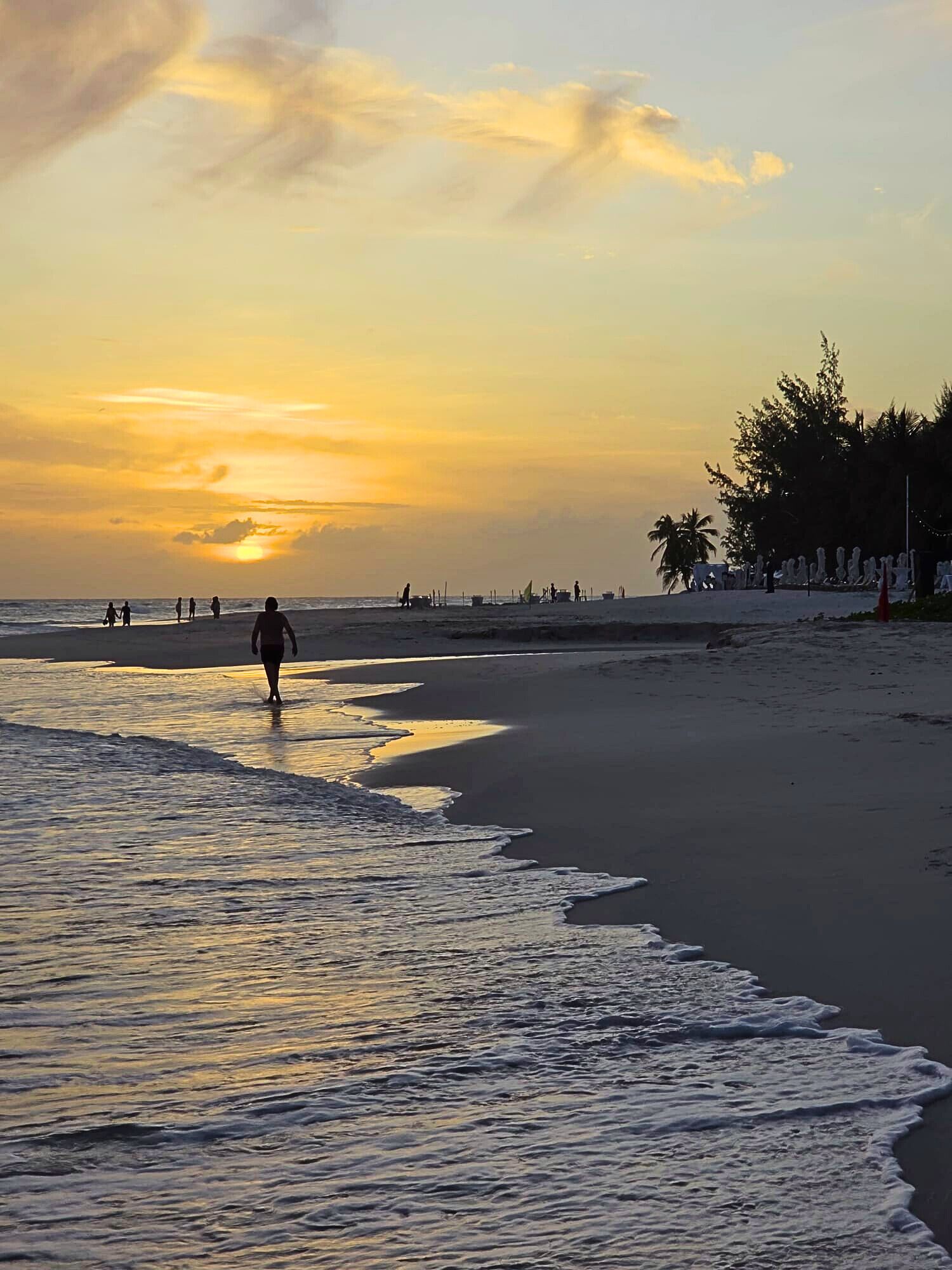 Een strand met een zonsondergang, rustige golven en mensen die wandelen.