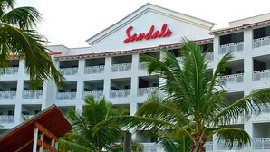 Een hotel met een opvallend 'Sandals' bord, meerdere balkons en palmbomen op de voorgrond.
