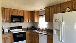 Cocina compacta con armarios de madera, microondas, estufa, lavavajillas y refrigerador.