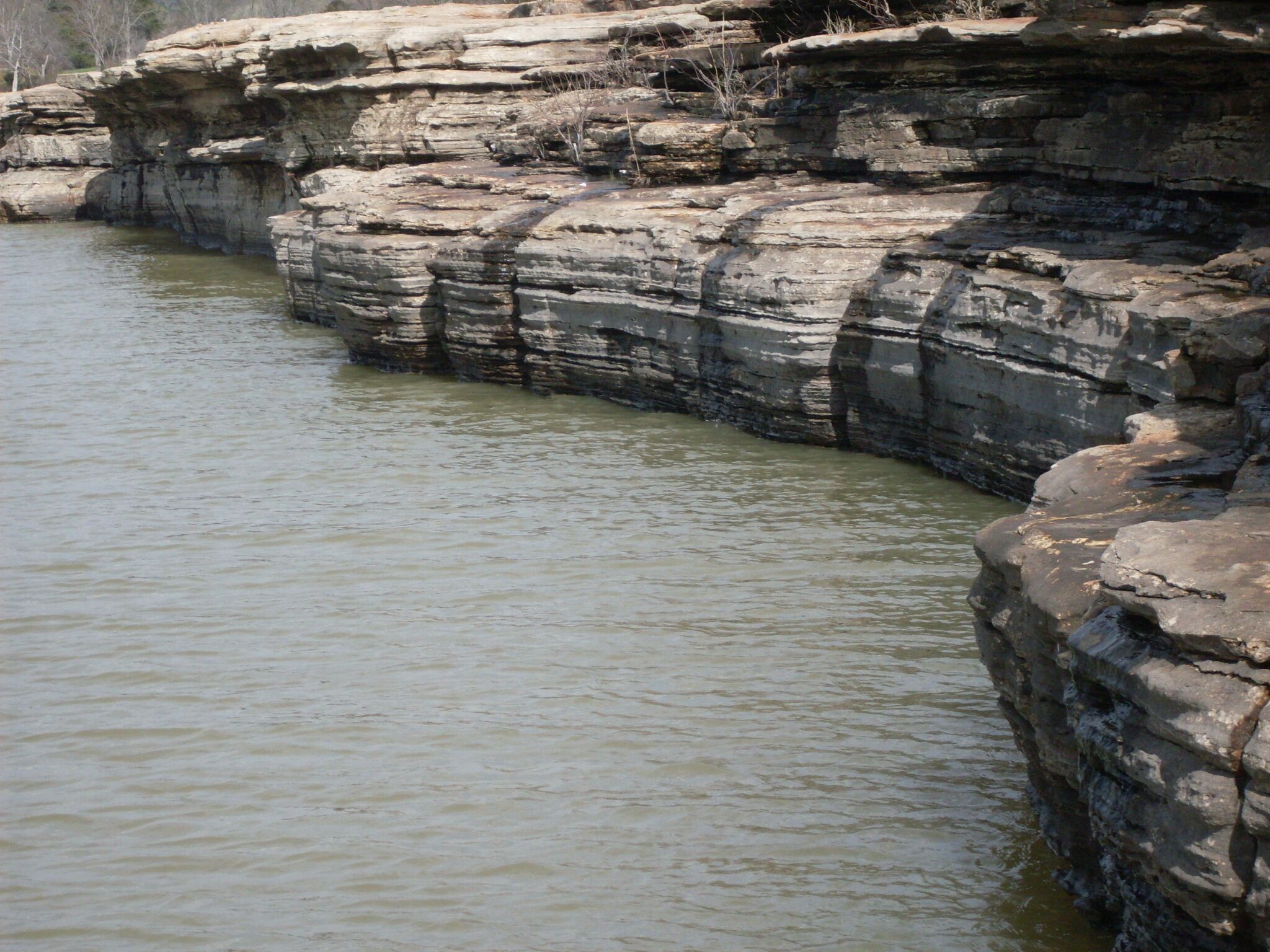 Orilla rocosa de un río con formaciones rocosas sedimentarias en capas.