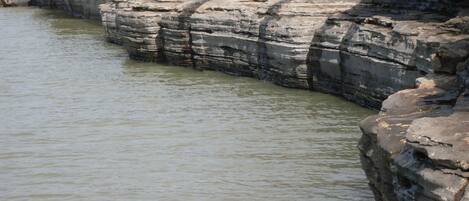 Orilla rocosa de un río con formaciones rocosas sedimentarias en capas.