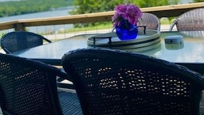 Una mesa redonda con sillas en una terraza que da a una masa de agua, con un jarrón de flores sobre la mesa.