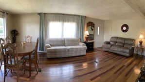 Una sala de estar con una mesa de comedor de madera, dos sofás y un amplio ventanal con cortinas.