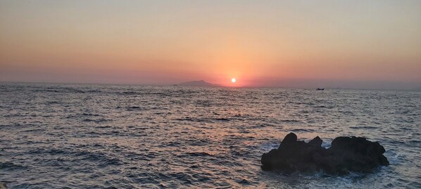 Atardecer sobre una masa de agua con un promontorio rocoso en primer plano.