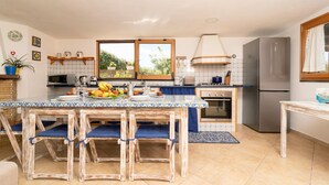 A kitchen with a central island, a stove, a refrigerator, and a window with a view of greenery.