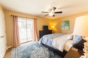 A bedroom with a bed, a ceiling fan, a TV, a lamp, and a window with curtains.