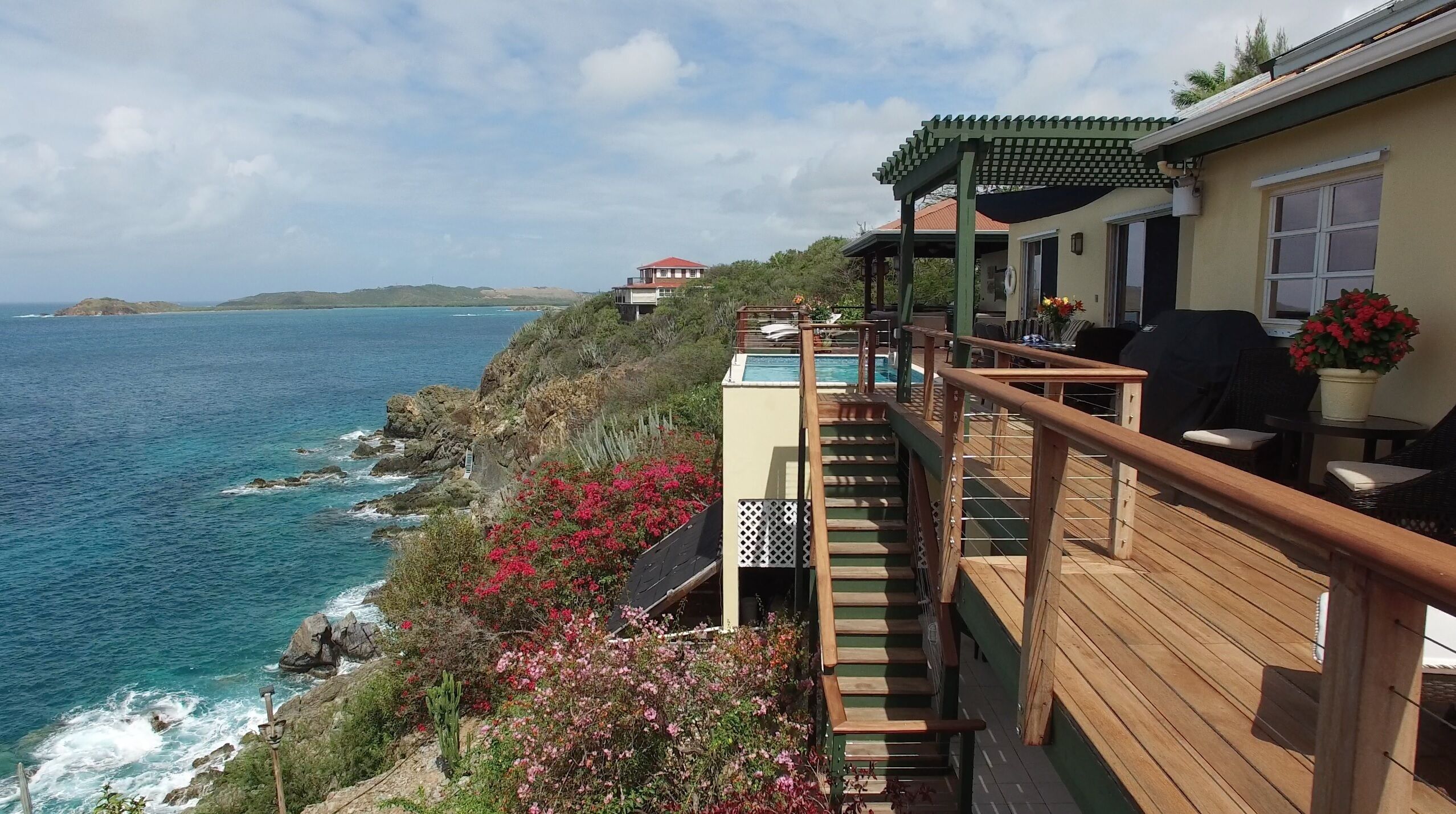 A wooden deck with a pool, overlooking the ocean.