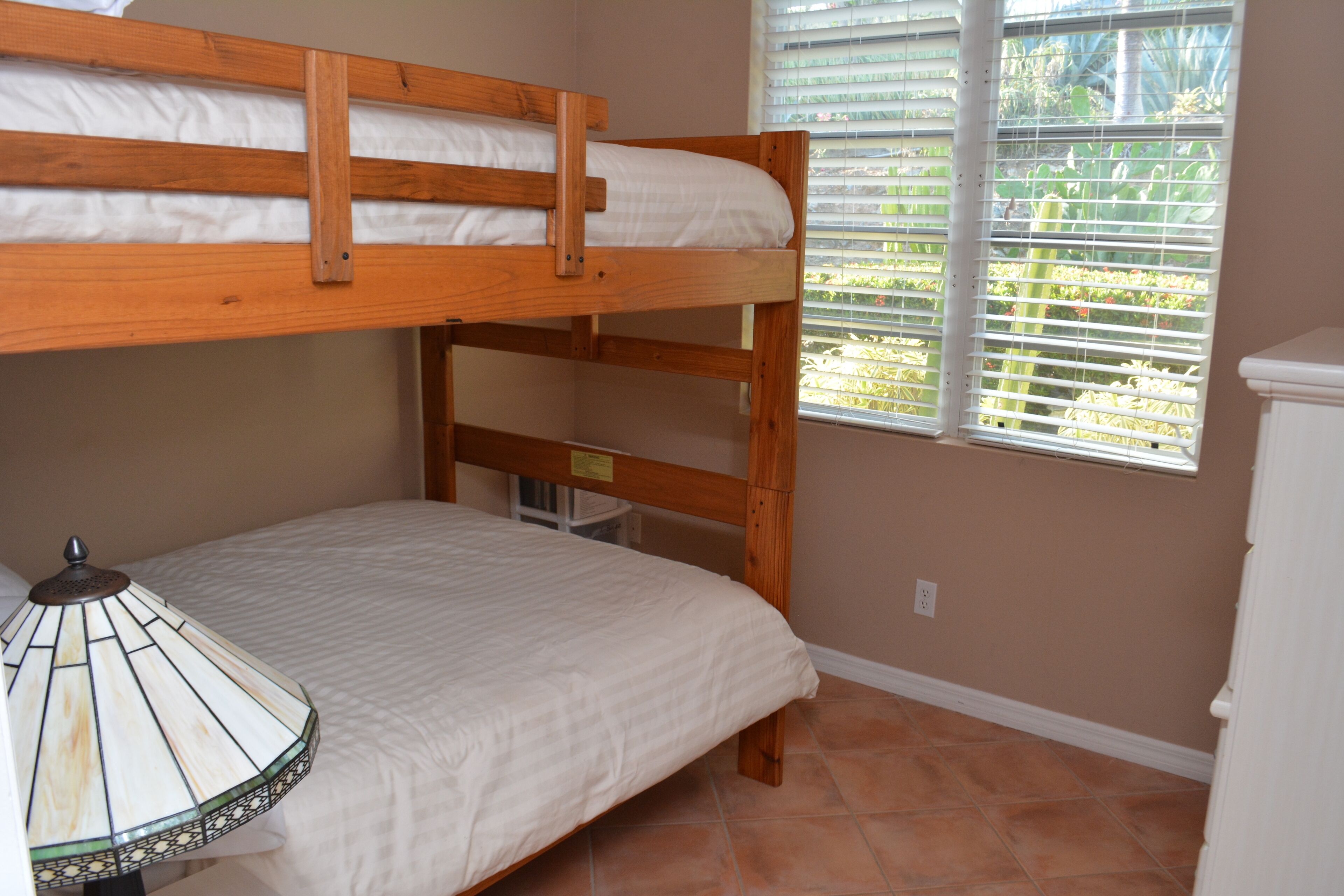 A bunk bed room with a lamp, a window with blinds, and a white cabinet.