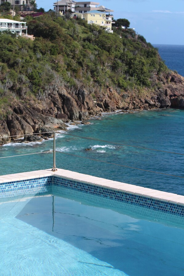 Relax by the tranquil pool overlooking the ocean with a stunning view of the coastline and lush greenery.