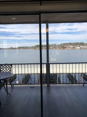 A balcony with a view of a calm body of water, a metal railing, and a table with chairs.