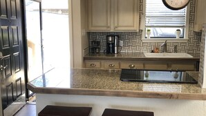 Una cocina con encimera de granito, taburetes de madera, un reloj colgante y una ventana con persianas.