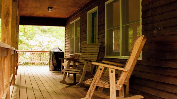 A wooden porch with rocking chairs and a grill, overlooking a green landscape. - Classic mountain cabin with beautiful stone fireplace in a rural setting (Plumtree)