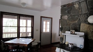 A kitchen with a stone wall, a stove, and a dining area with a table and chairs. - Classic mountain cabin with beautiful stone fireplace in a rural setting (Plumtree)