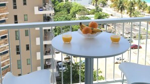 A balcony with a table and chairs, overlooking a beach and cityscape.