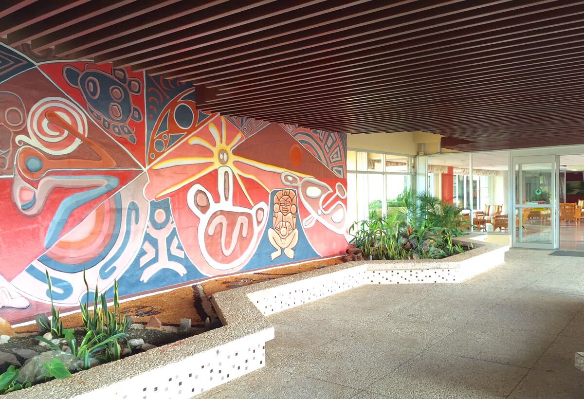 Une entrée moderne, agrémentée d’une fresque colorée, d’un espace extérieur abrité et d’un coin salon avec des chaises et des tables.