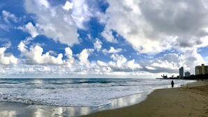 A beach with waves, a clear sky, and buildings in the background.
