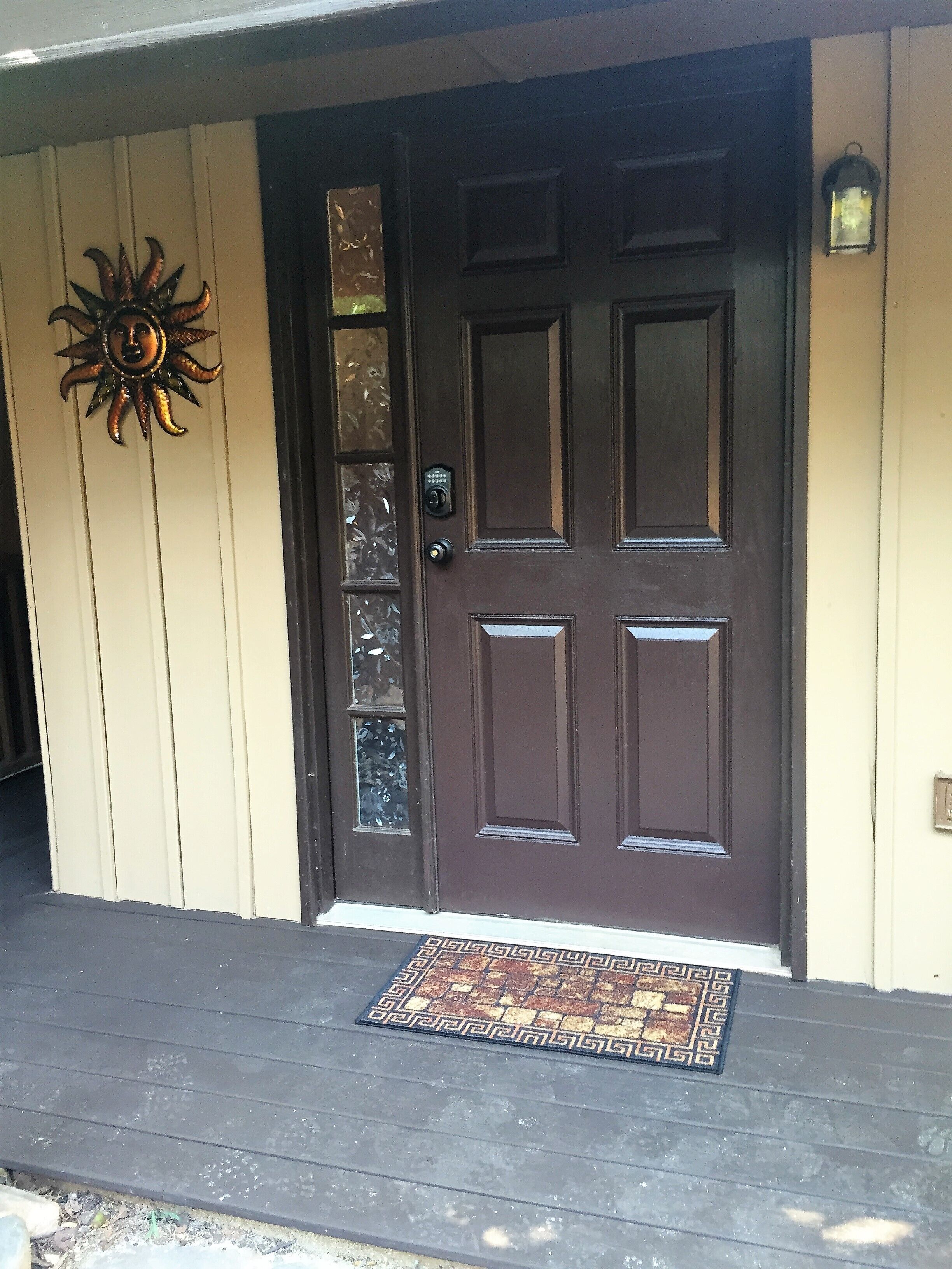 A dark brown door with a glass panel, a doormat, and a sun decoration on the wall.