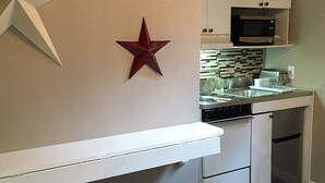 A modern kitchen with white cabinetry, a microwave, and a built-in oven. There are two wooden stools and a decorative star on the wall.