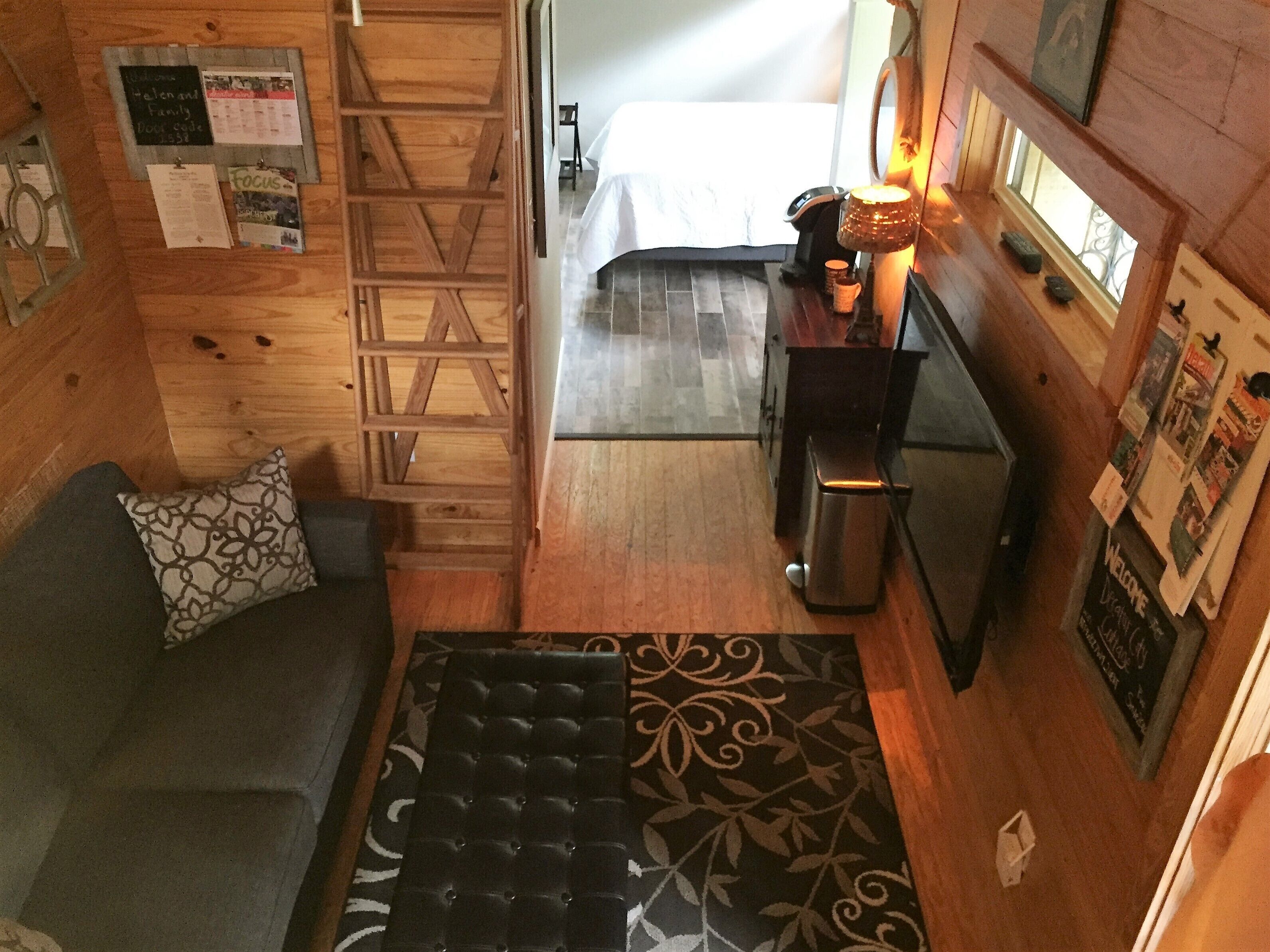 Een gezellige kamer met houten inrichting, een bed, een bank, een klein tafeltje met een lamp en een prikbord met verschillende berichten.