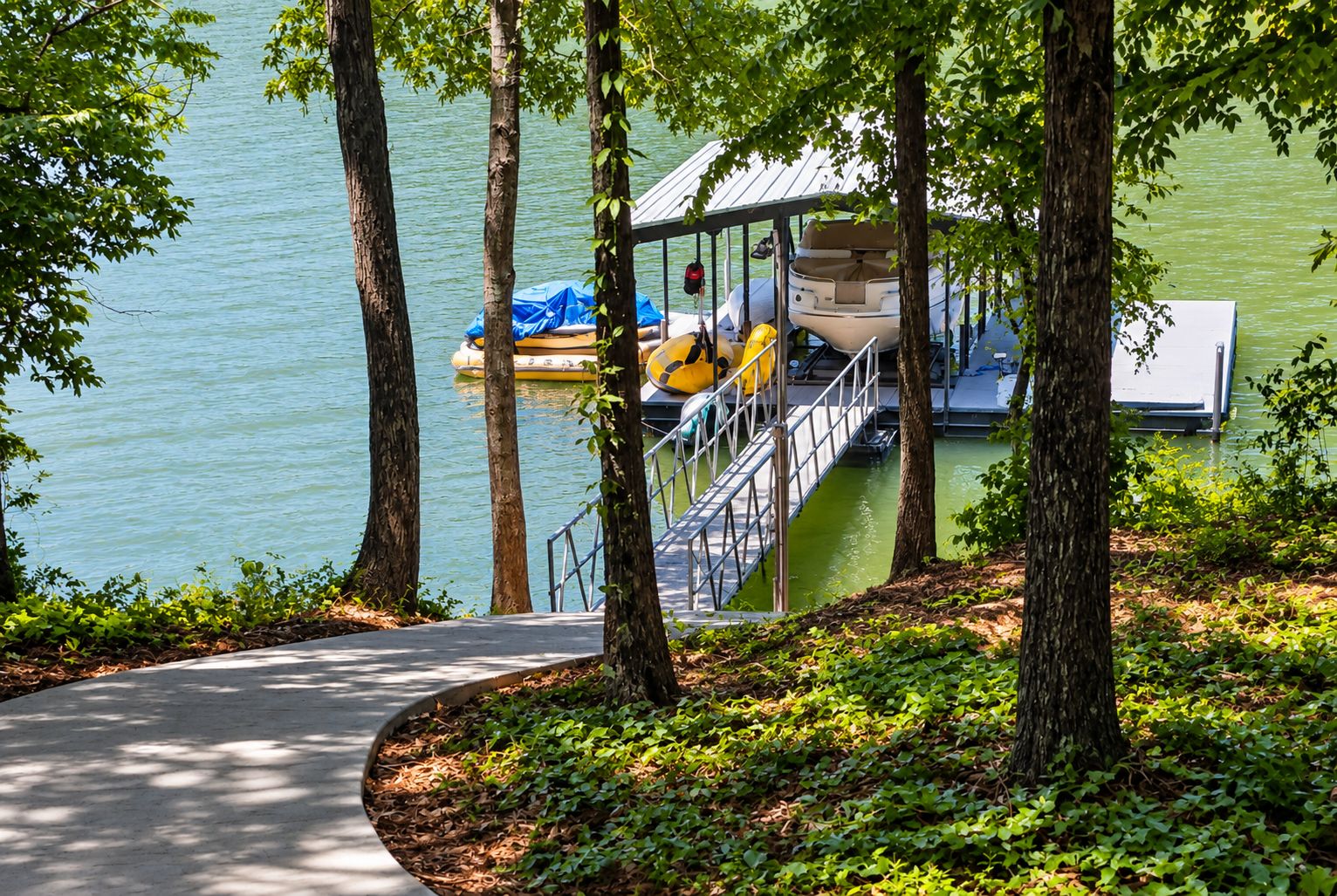 A dock with a boat and a covered area, surrounded by trees and a pathway.