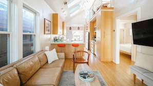 A modern living room with a sofa, a coffee table, and a TV. There is a kitchen area with a dining table and chairs.