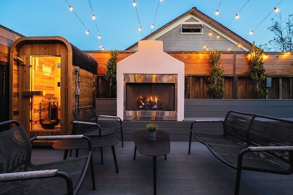 Une terrasse extérieure dotée d’une cheminée en pierre, de sièges et de guirlandes lumineuses.