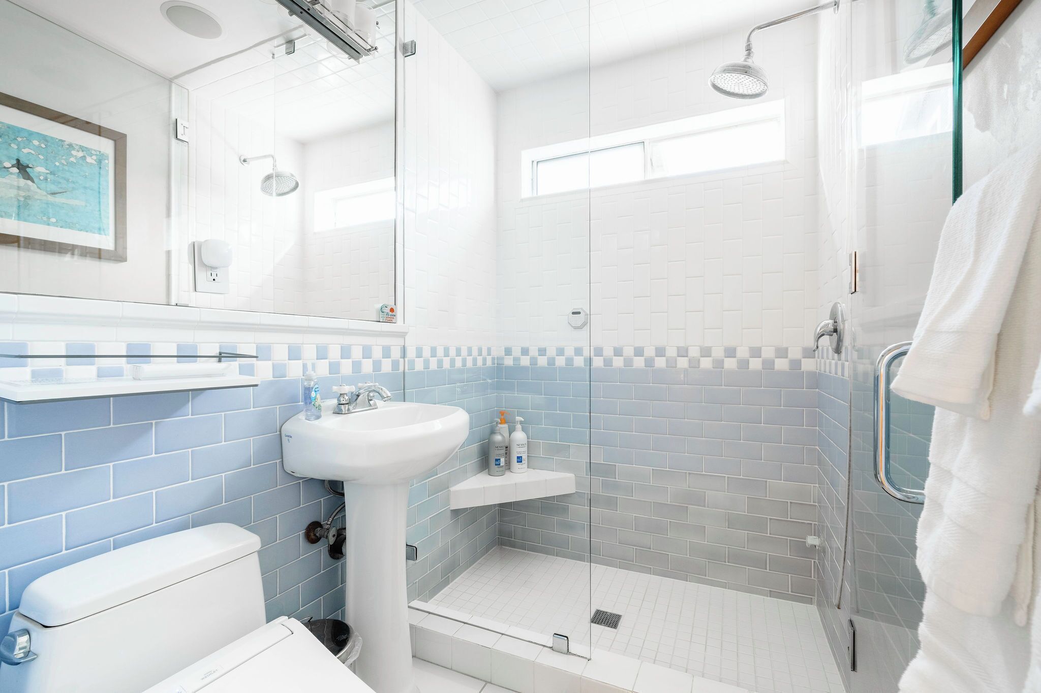Een moderne badkamer met een douchecabine van glas, een witte wastafel en een doucheruimte betegeld met blauwe tegels.