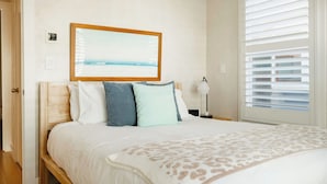 A bedroom with a bed, a nightstand, a lamp, a window with blinds, and a framed picture on the wall.