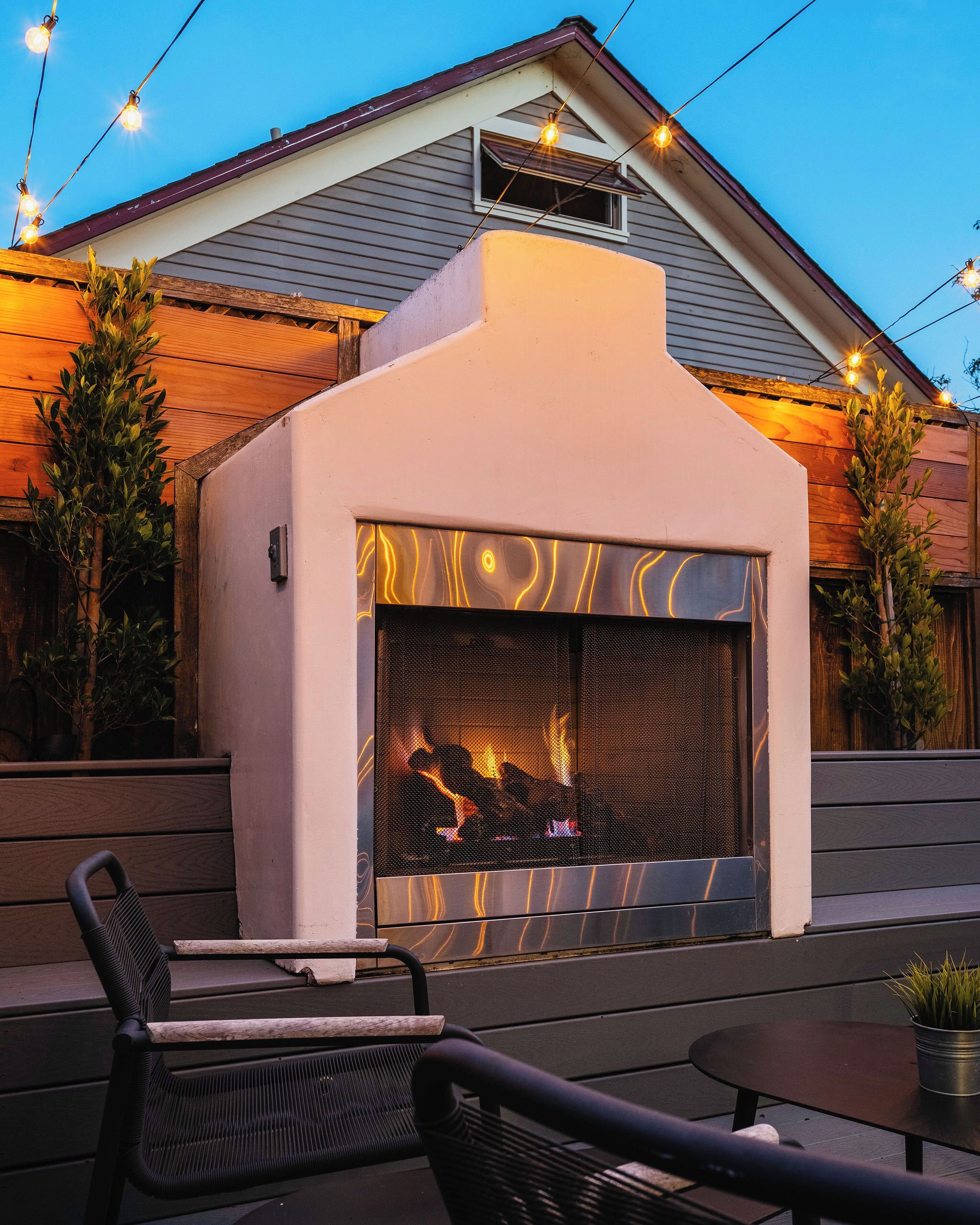 An outdoor patio area with a built-in fireplace, seating, and string lights.