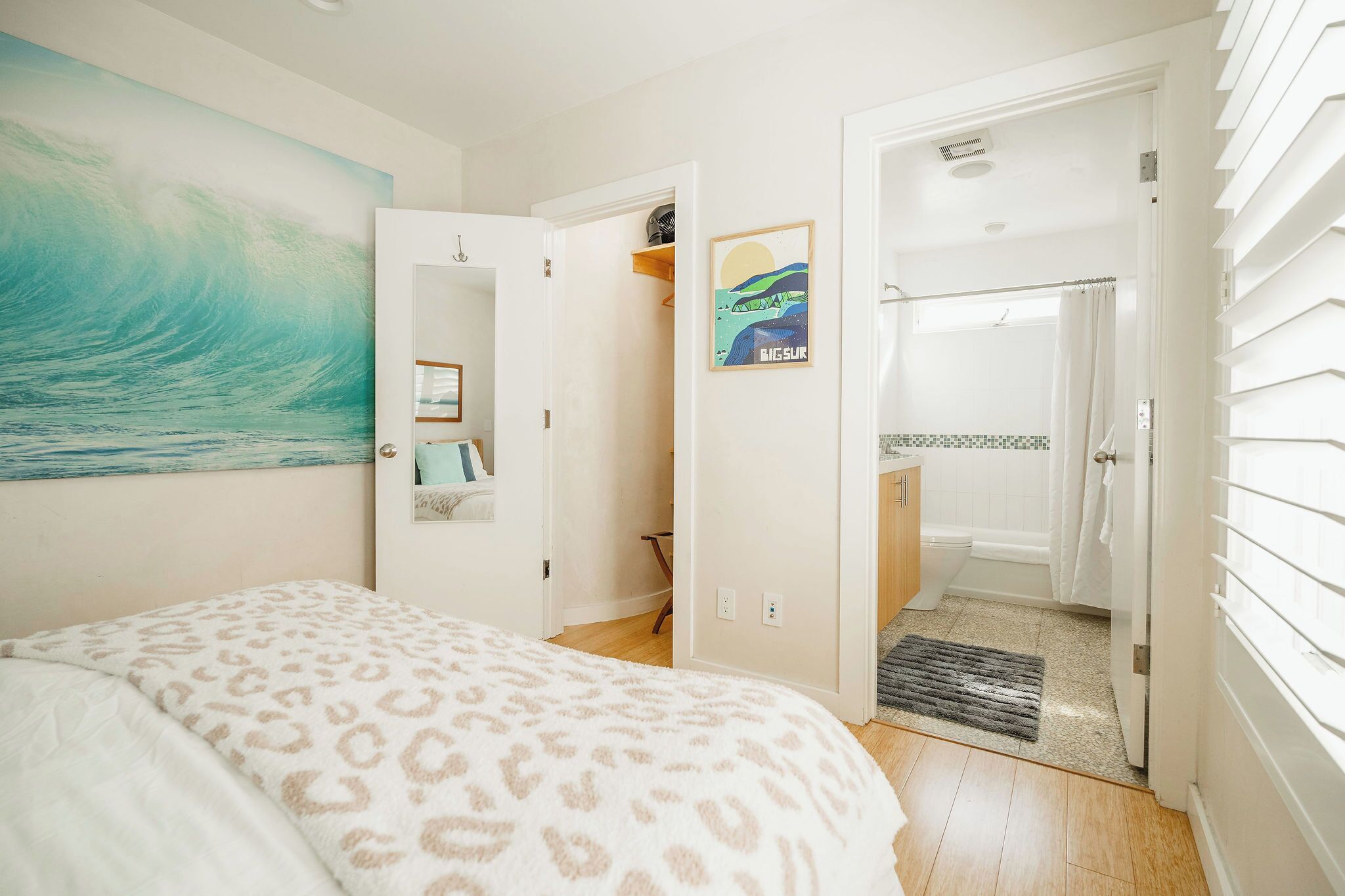 A bedroom with a bed, a large wave painting, a closet, and a bathroom with a shower and toilet.