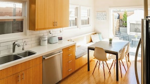 A modern kitchen with wooden cabinets, a built-in dishwasher, and a dining area with a table and chairs.