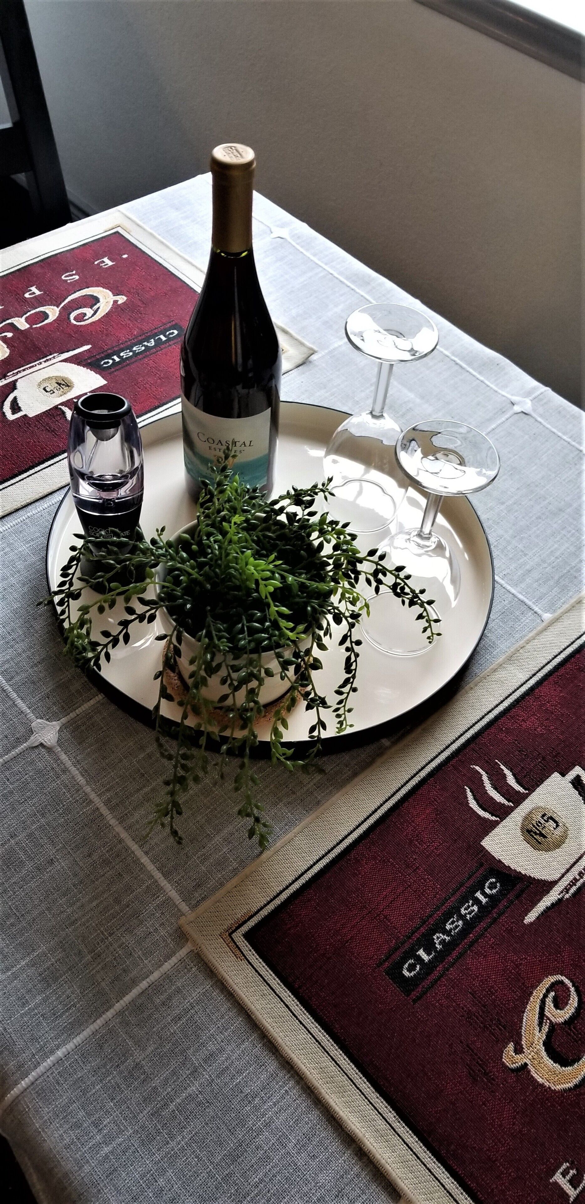 Una mesa dispuesta con una botella de vino, copas y una planta decorativa.