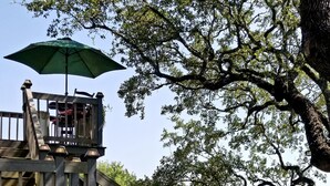 Una terraza de madera con un parasol verde, un pequeño puente y un estanque con peces.