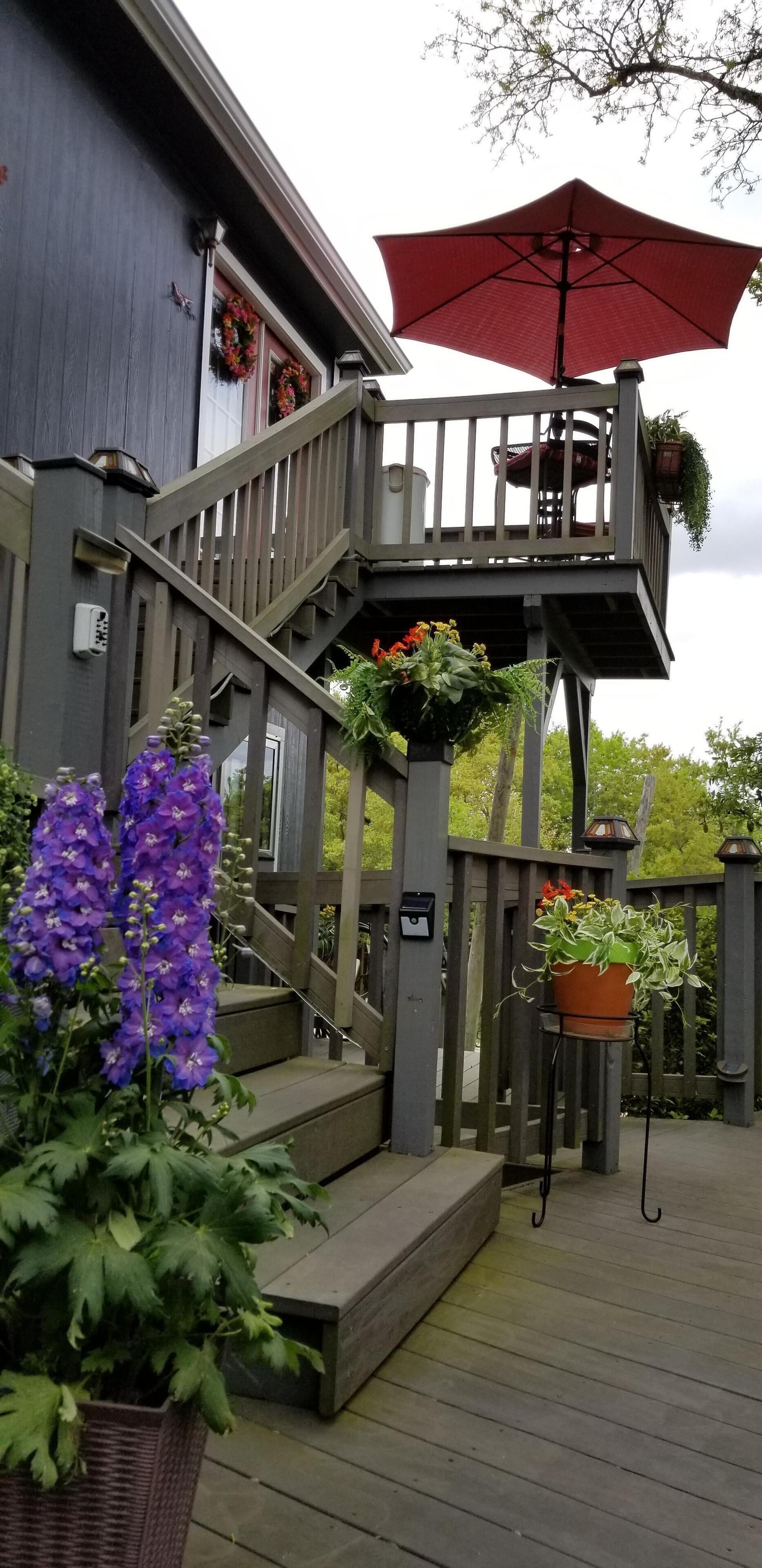 A wooden deck with a staircase leading to a balcony, potted plants, and a red umbrella.