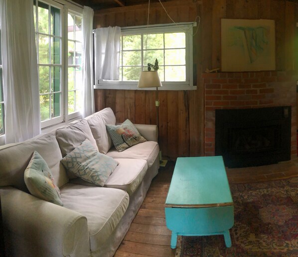 A cozy room with a wooden floor, a beige sofa with patterned cushions, a teal coffee table, and a fireplace.