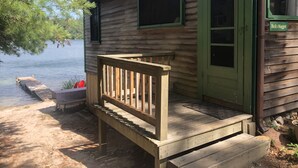 Eine Holzhütte mit grüner Tür und Fenstern, einer hölzernen Bank und einem Steg, der in einen See führt.