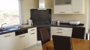 Una cocina moderna con armarios blancos, encimera negra y una mesa de comedor de madera con sillas.