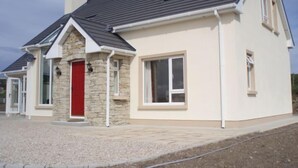 Una casa moderna con fachada de piedra, una puerta roja y un techo gris.