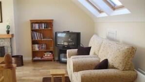 Un salón acogedor con un sofá, una mesita, una estantería y un televisor.
