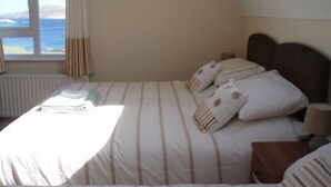 Un dormitorio con cama, ventana con cortinas y vista al mar.